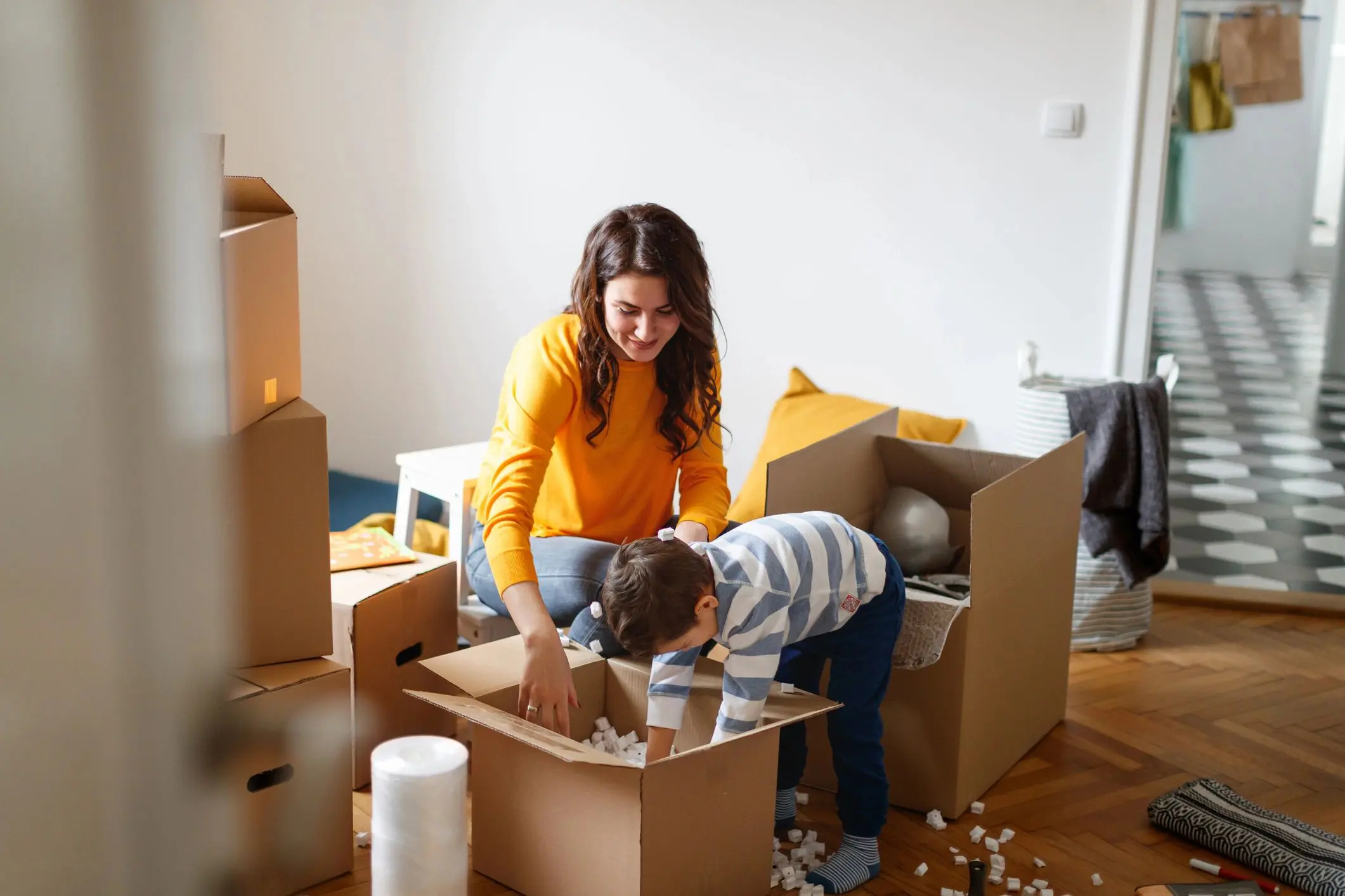 Toddler playing with his mother during house move, digging into cardboard box for packing peanut to throw around